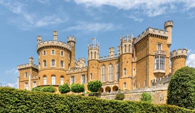 The exterior of Belvoir Castle seen from above a large hedge in the gardens.