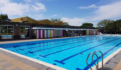 An outdoor swimming pool on a sunny day, with buildings in the background.