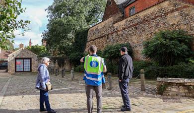 A male tour guide offering information about a Roman wall to two adults
