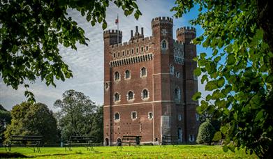 A view of Tattershall Castle rising from the Lincolnshire Fens, surrounded by trees.