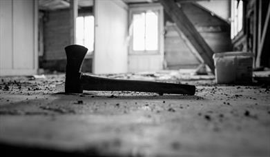 Image shows an axe on the ground of an abandoned barn, as part of a murder mystery event